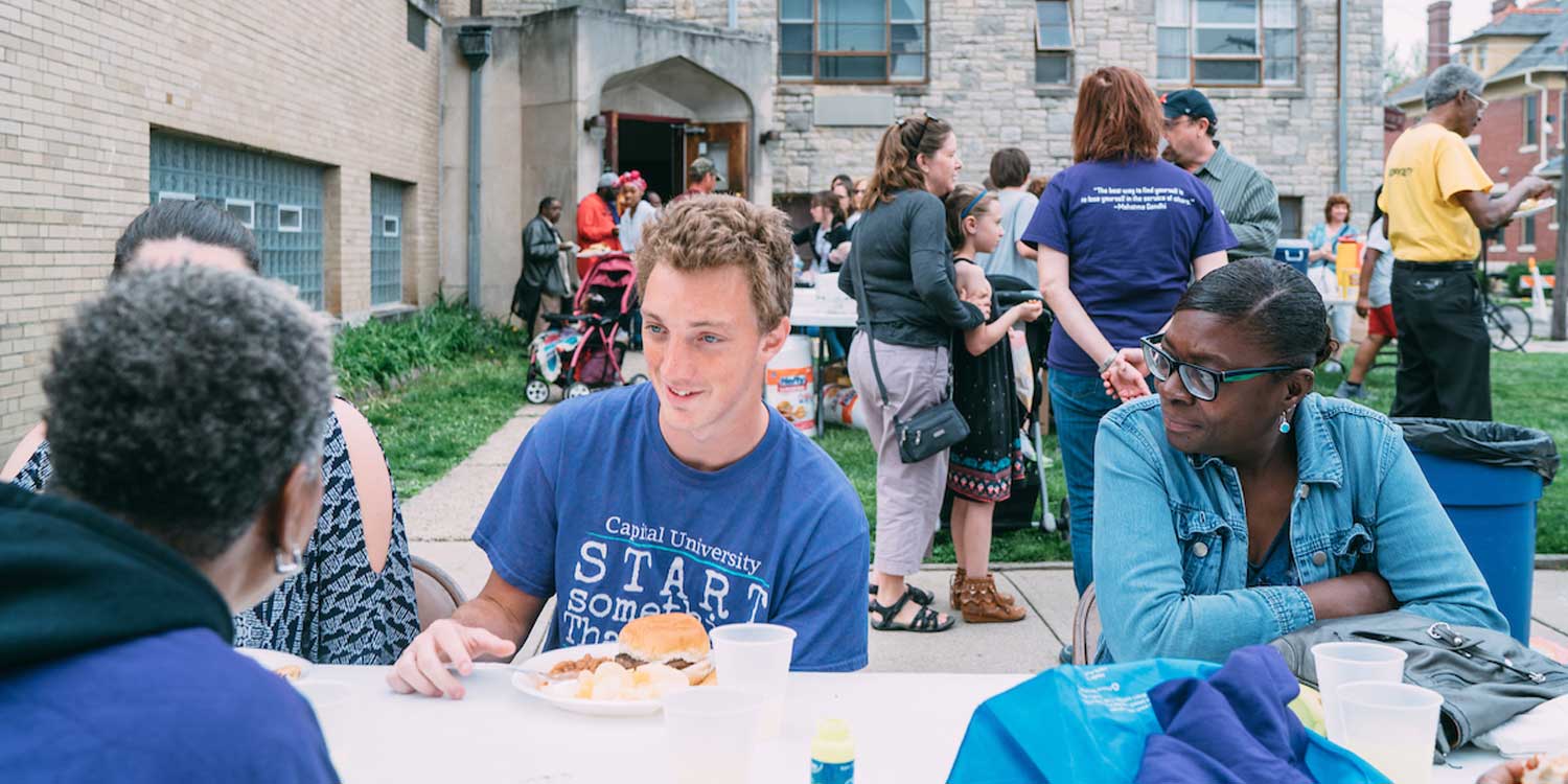 capital students eating at picnic table outside at a block party