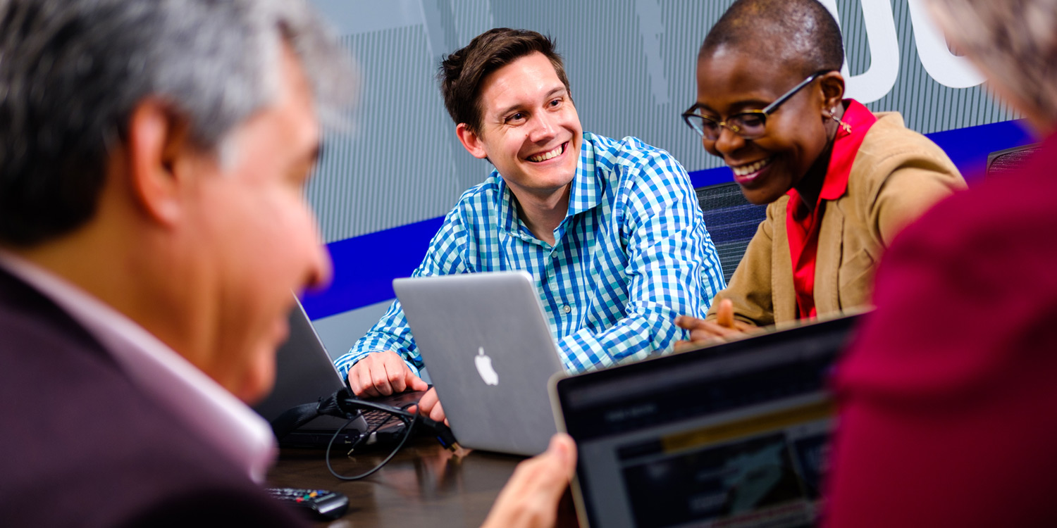 smiling adult student sitting at table with other adult students in front of their laptops