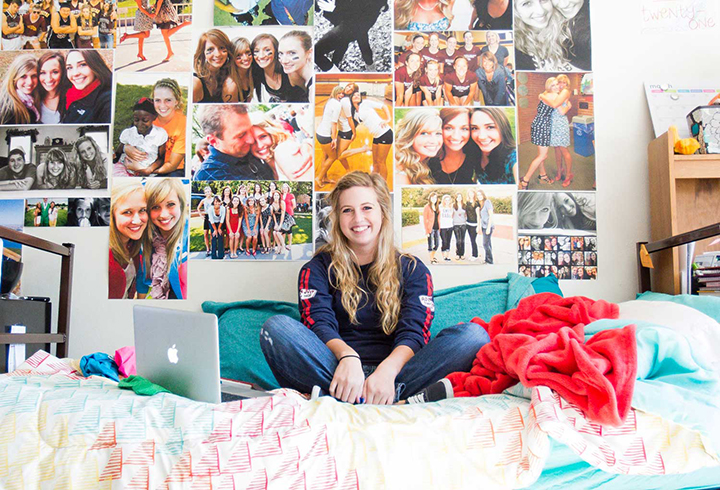 Student sitting on bed in dorm room