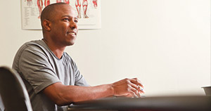 man with shaved head in gray short sleeve shirt sitting at desk